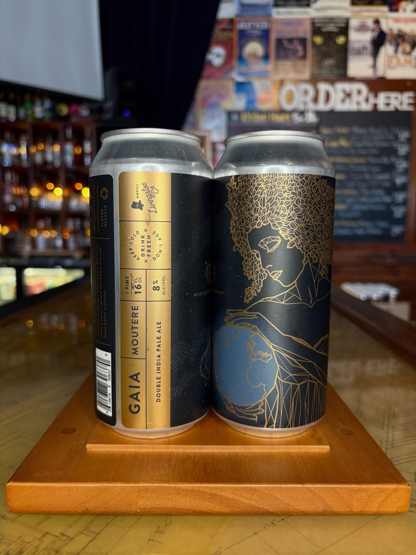 Two craft beer cans displayed on a wooden stand at a bar counter.